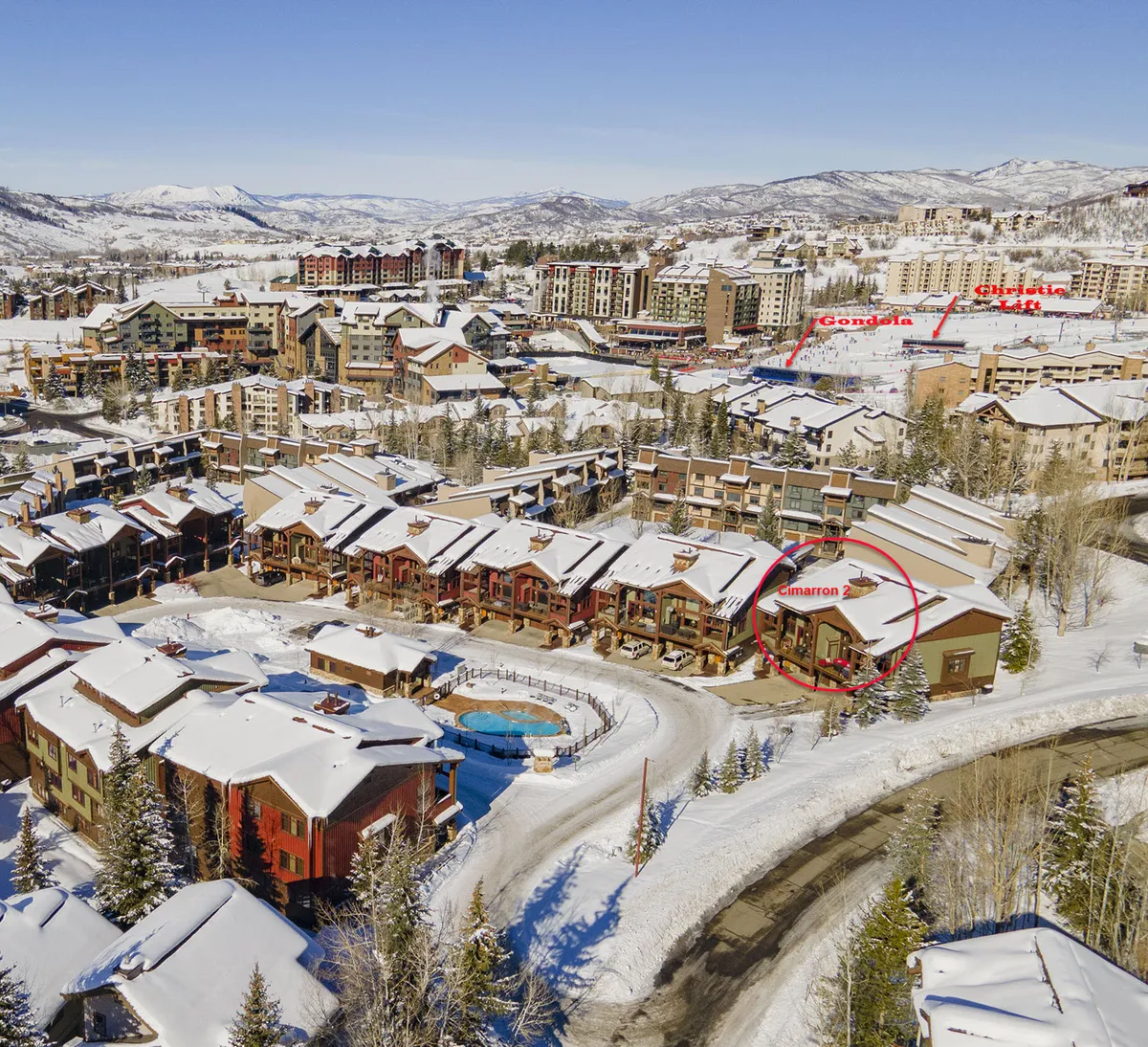 A circular pool sits amid a picturesque, snow-dusted setting, framed by townhome rooftops and scenic mountains in the background. The setting feels cozy yet exclusive, evoking a sense of seasonal convenience and après-ski relaxation. The snowy landscape hints at the resort's appeal during ski season and the ease of returning to such amenities after a day of adventure.