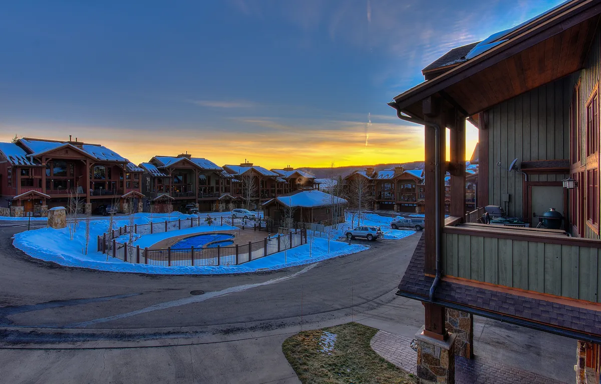 A snow-covered swimming pool area surrounded by buildings, with a glowing sunset sky in the background. The pool is the focal point, with the winter setting creating a cozy and inviting après-ski atmosphere. Lounge chairs and winter-clad guests are visible, suggesting relaxation and group gatherings after a day of adventure.