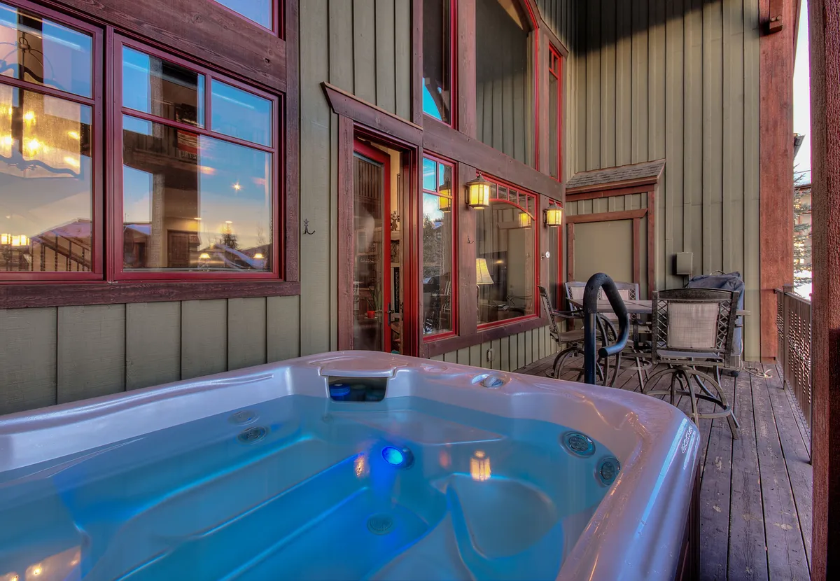 A private deck featuring a bubbling hot tub and comfortable outdoor seating, set against large windows. The space is perfect for relaxing evenings, sharing stories, or soaking under the stars in the fresh alpine air.