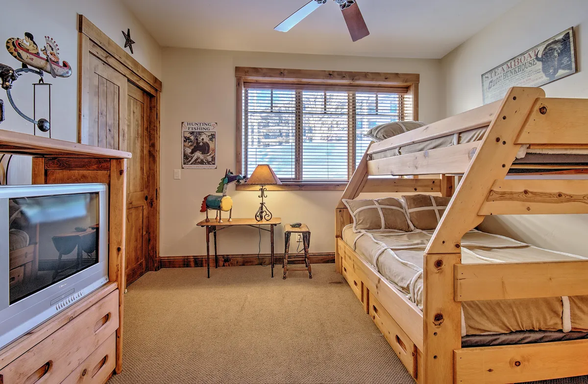 A warm, family-friendly bunk bedroom with twin-over-full bunk beds, wooden furniture, a lamp, and cheerful wall art. The room is inviting, designed for sleepovers, reading, or games—perfect for children or groups.
