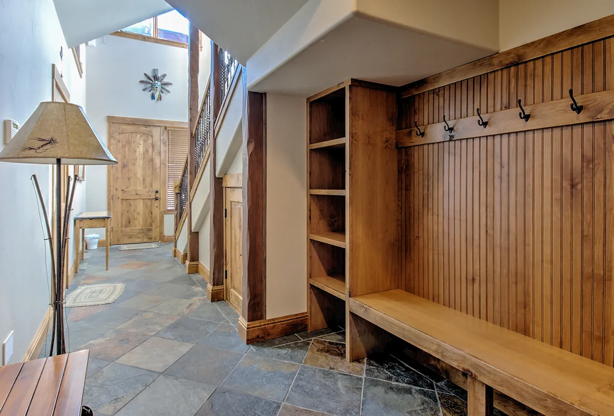 This image captures a functional and inviting entryway featuring a wooden bench, coat hooks, slate flooring, and a staircase leading upstairs. The area is designed for guests to comfortably remove and store outdoor gear after a day of activities, with ample space for shoes and coats.