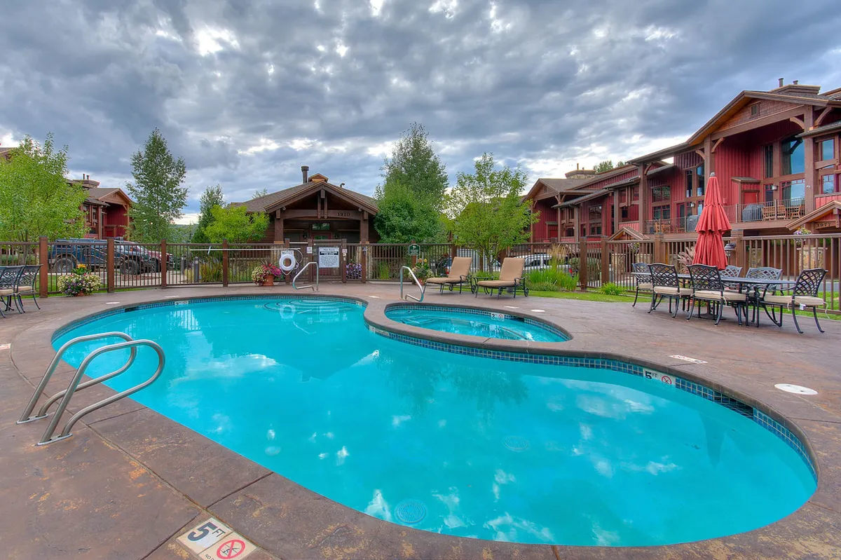 A vibrant exterior scene featuring the community swimming pool, a relaxing hot tub, lounge chairs with umbrellas, and verdant greenery. The layout encourages sunbathing, social gatherings, and tranquil moments surrounded by nature.