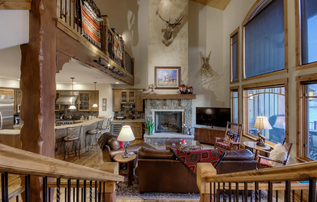 A spacious living area with a warm fireplace, plush sofa, soaring ceilings, and expansive windows that fill the space with brilliant mountain light. Antler decor and wood accents add rustic charm, while the room feels open and inviting for gatherings.