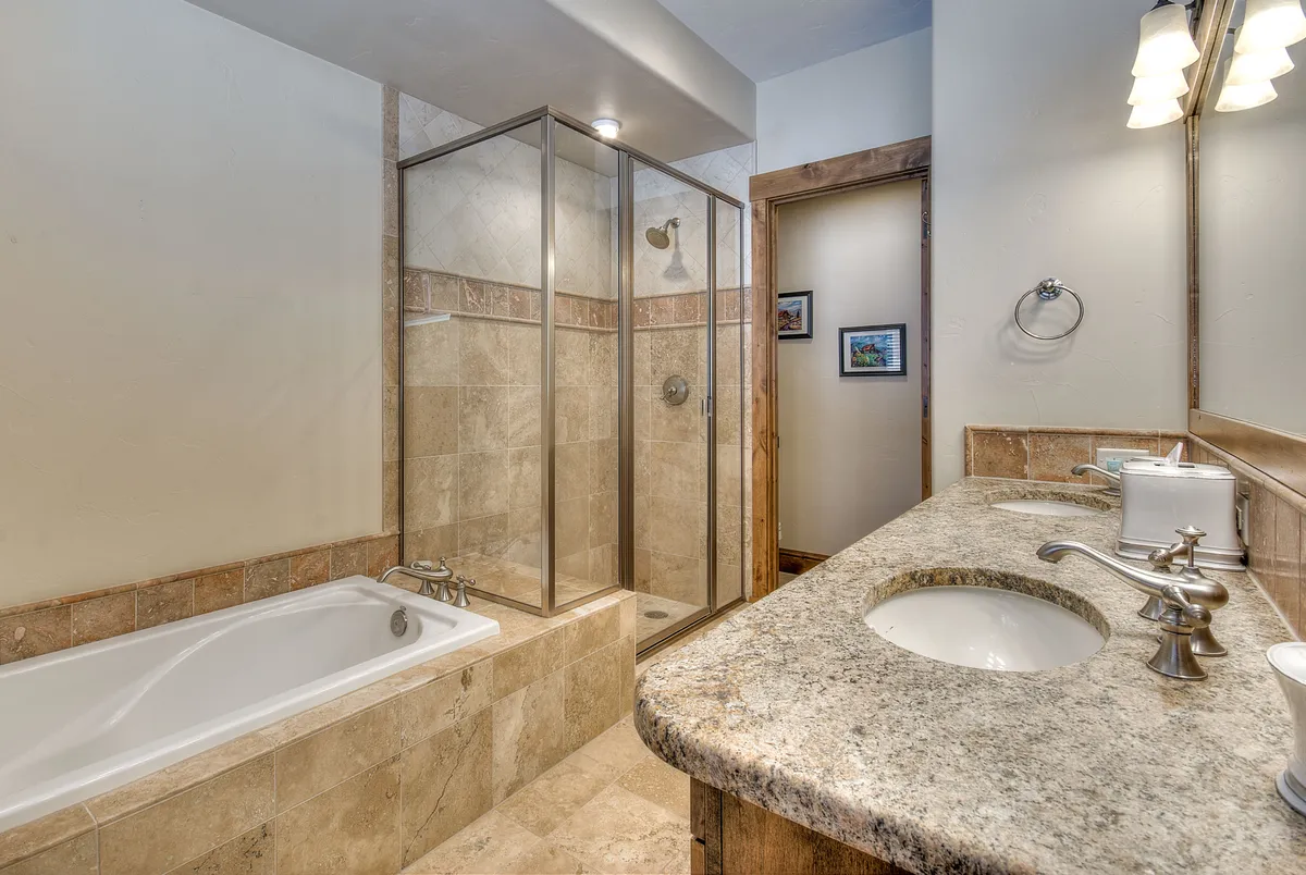 A serene bathroom with a luxurious bathtub, walk-in shower, double vanity, and a large mirror. The calm, inviting atmosphere is perfect for unwinding after a long day.