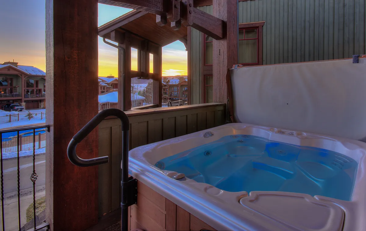 A serene hot tub is perched on a balcony with a stunning sunset view. The scene suggests privacy and tranquility, ideal for soaking after a day of activities. The outdoor setting blends exclusivity with the comfort of resort-style living, and the warm glow of the sunset highlights the luxurious experience.