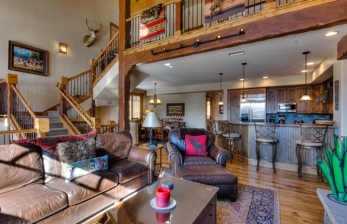 An open-concept layout featuring a comfortable living area with leather couches, a view of the adjacent kitchen area, a decorative staircase, artwork, and a prominent dining table ideal for family meals or game nights.