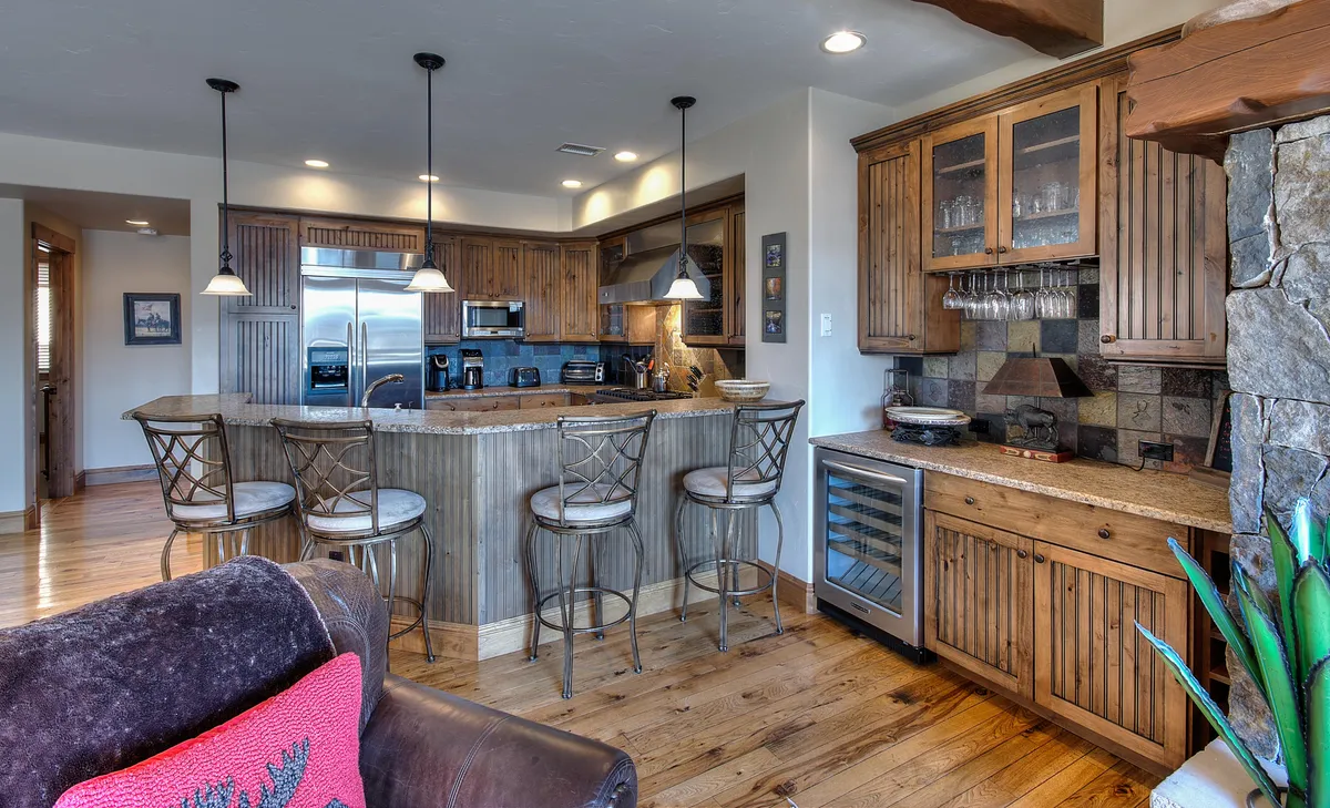 A well-appointed kitchen featuring a large island with bar stools, warm wood cabinetry, and stone accents, designed for cooking and entertaining. The layout invites guests to gather while meals are prepared.