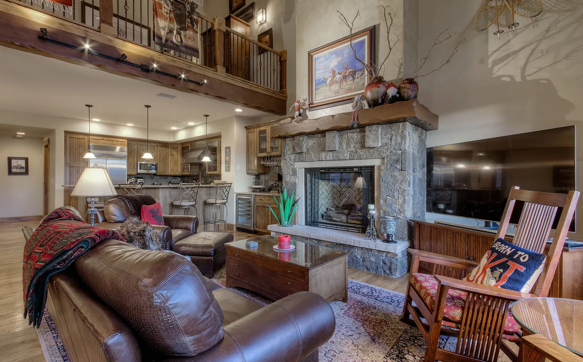 A warm, sociable living area with a glowing fireplace, plush sofas, vibrant artwork, and a glimpse of the dining area. This space invites gathering after a day spent outdoors, whether in winter or summer, and evokes a sense of relaxation and togetherness.